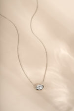 Silver east-west oval bezel pendant necklace arranged on a cream background.