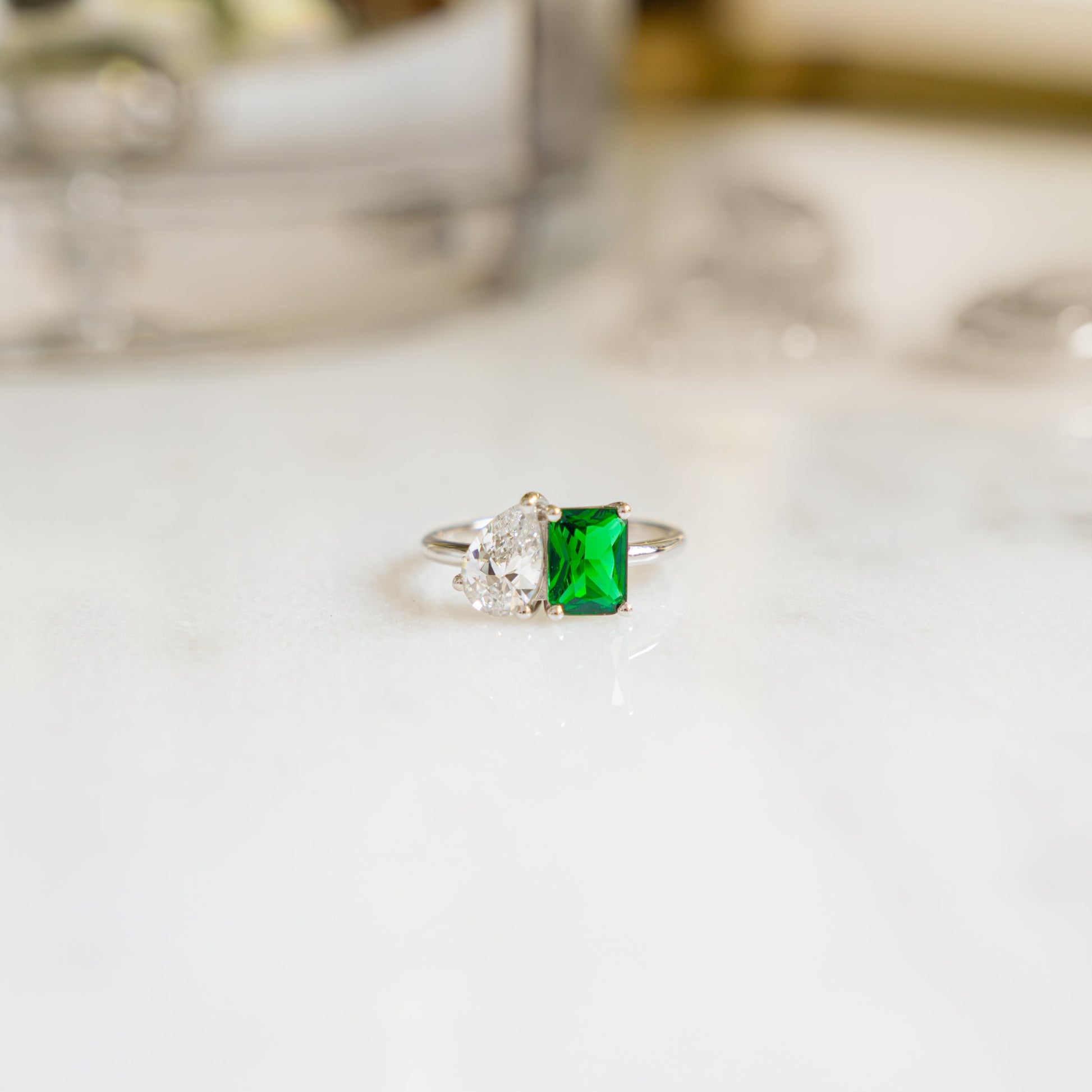 close up of a two stone ring with an emerald gemstone and a diamond pear shaped stone