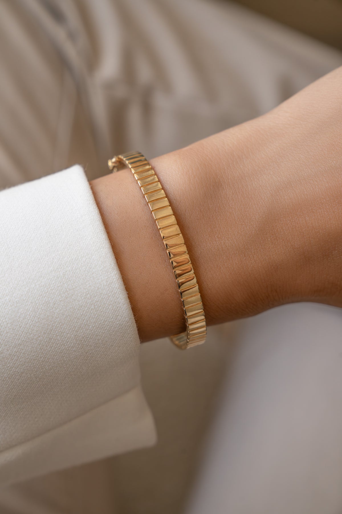 Gold fluted bangle worn alone on a model's wrist with a white shirt.