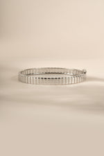 Silver fluted bangle resting on a cream background.