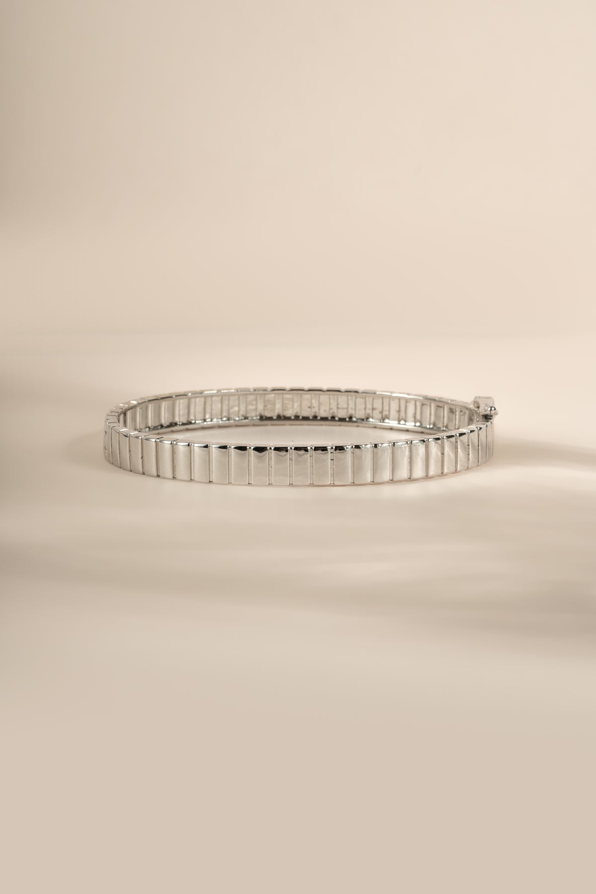 Silver fluted bangle resting on a cream background.