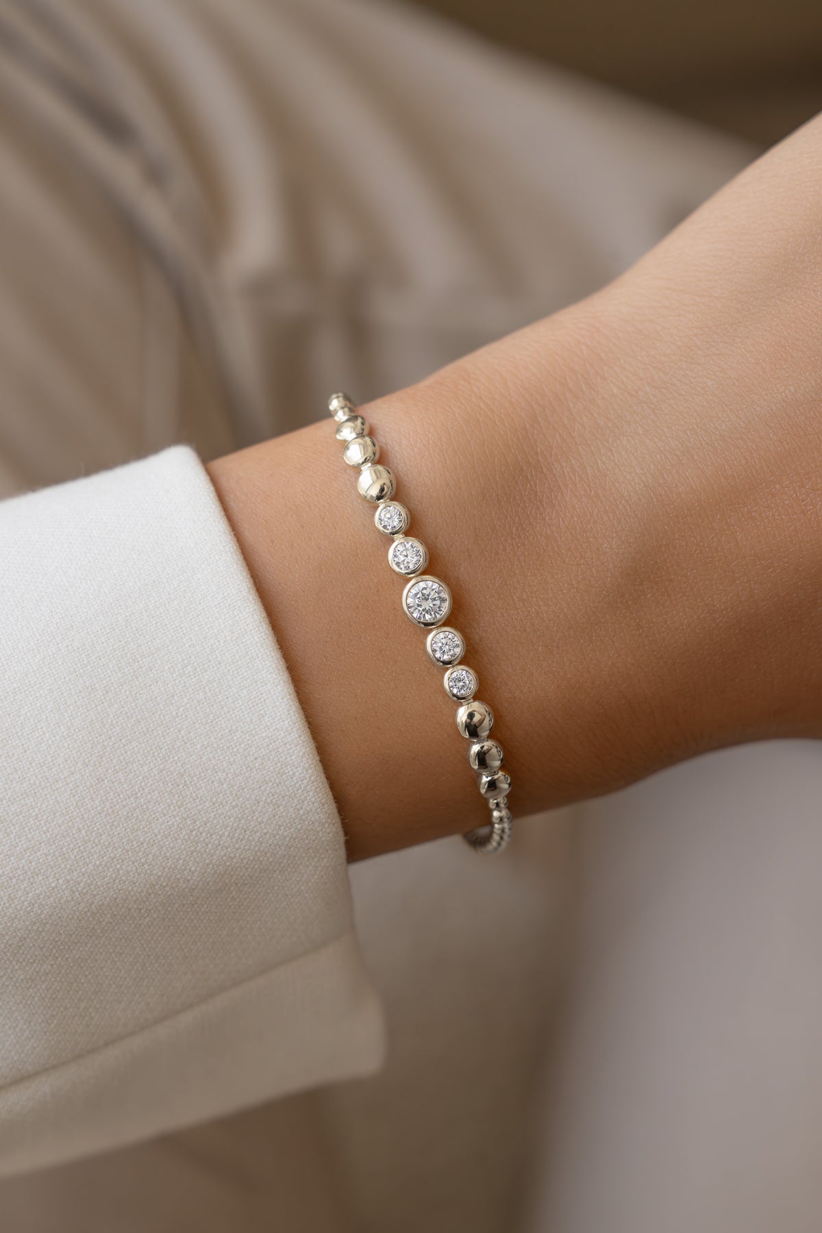 Silver graduated bezel tennis bracelet worn alone on a model's wrist.