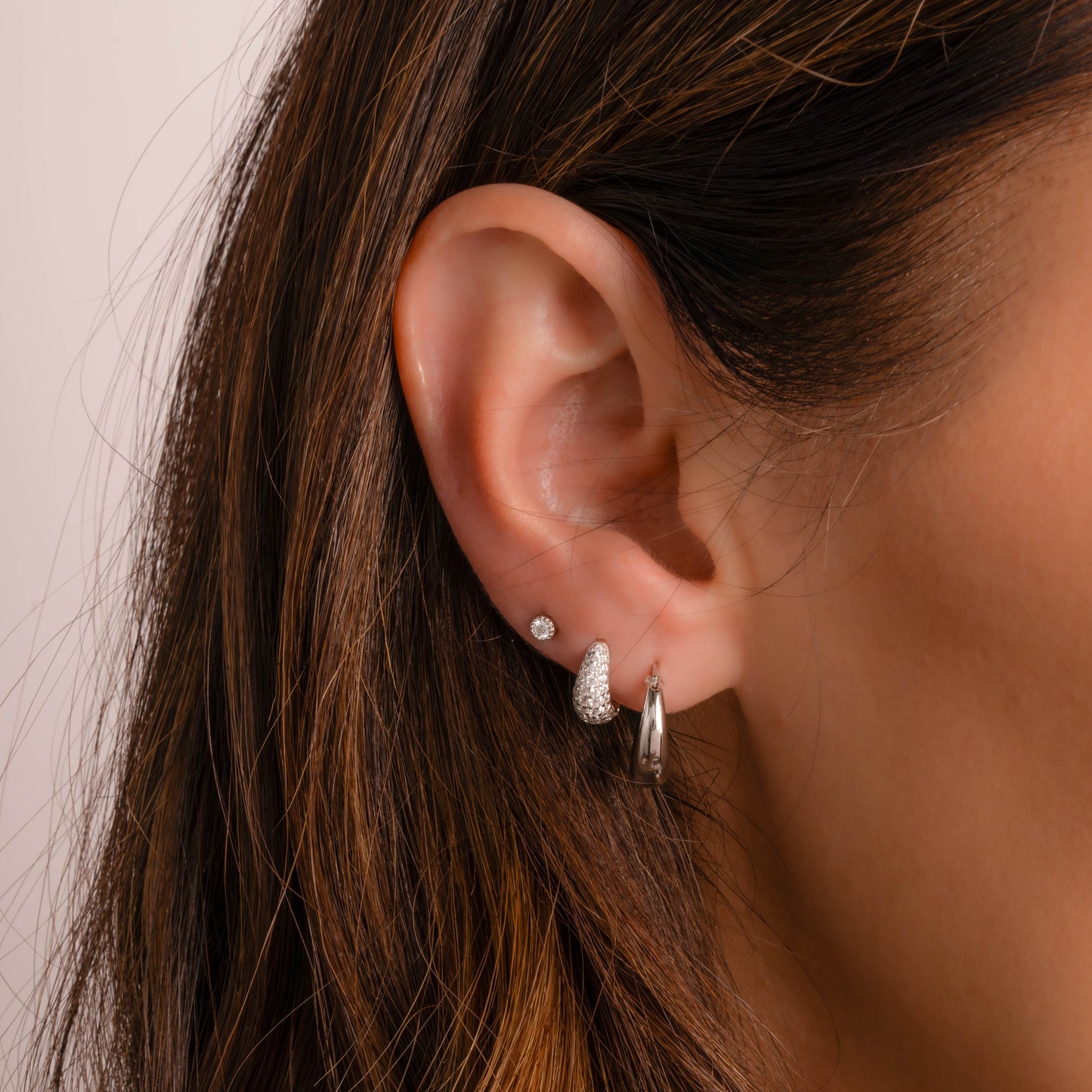 Model wearing silver huggie hoop earrings with tiny pave diamonds along with other silver earrings from Sami Jewels