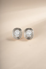 Front view of silver oval bezel statement studs on a cream background.