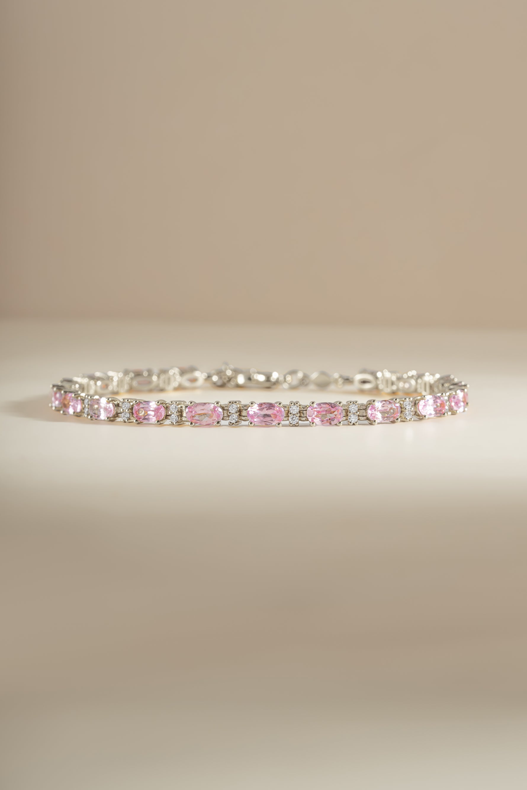 A silver tennis bracelet featuring a row of alternating pink oval gemstones and white round diamonds.