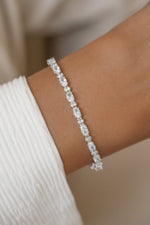 A close-up of a silver diamond tennis bracelet with oval and round stones.
