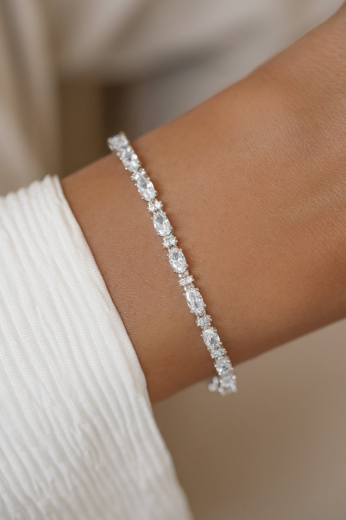 A close-up of a silver diamond tennis bracelet with oval and round stones.