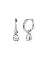Pair of rhodium silver huggie earrings with clear cubic zirconia pear-shaped charms on a white background.