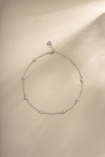 Silver Bezel Set Station Anklet laid flat on a warm neutral background.