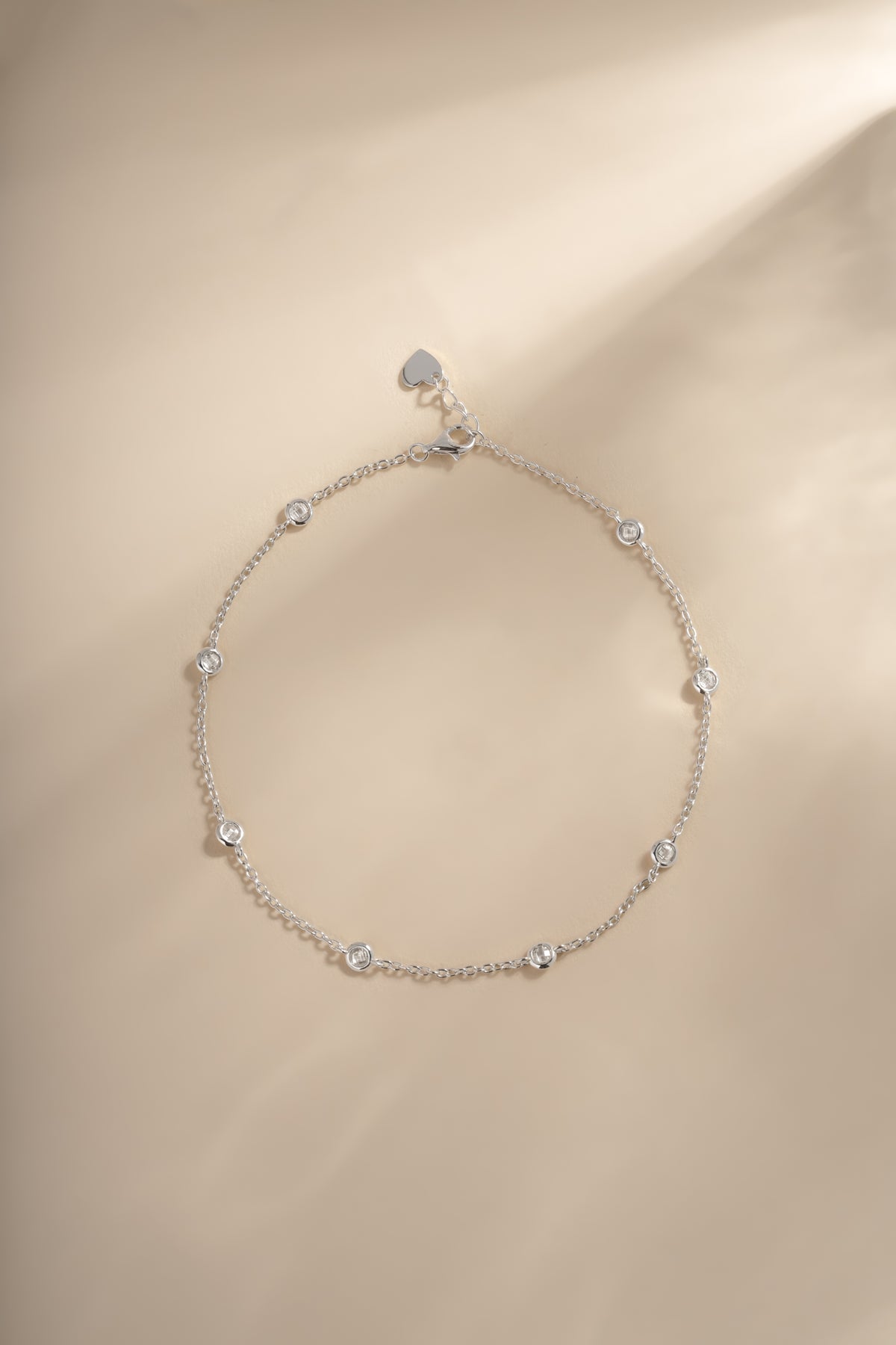 Silver Bezel Set Station Anklet laid flat on a warm neutral background.