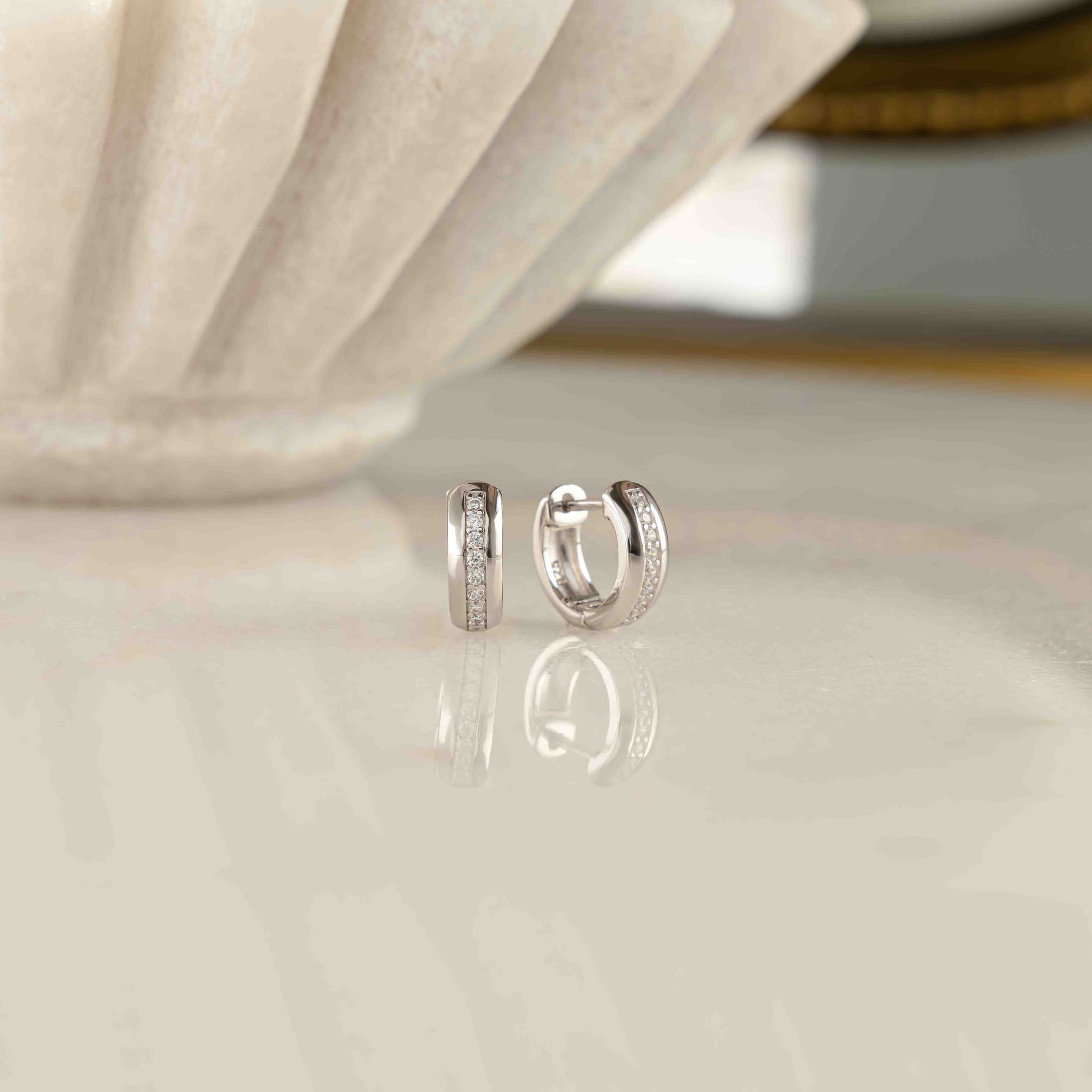 A pair of silver huggie earrings featuring diamond stones