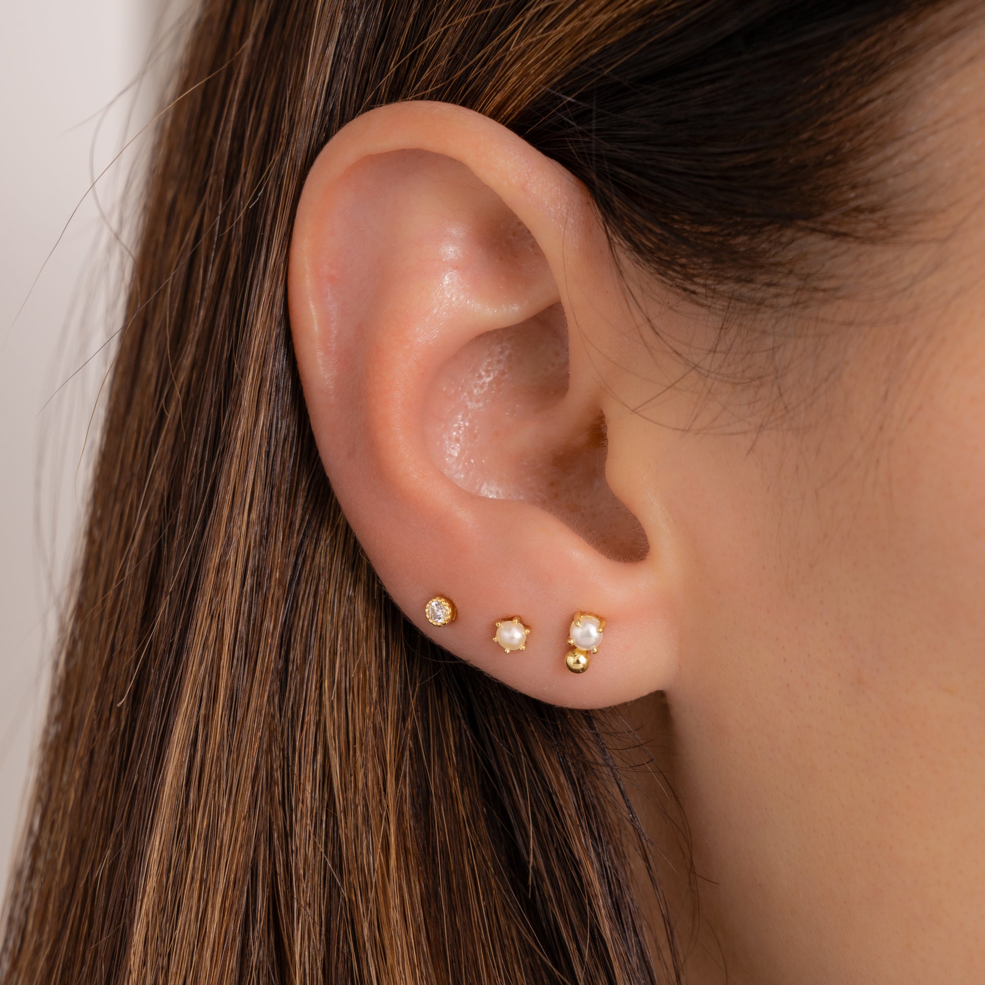 close up of model wearing diamond stud earrings in the third piercing stacked with opal studs. 