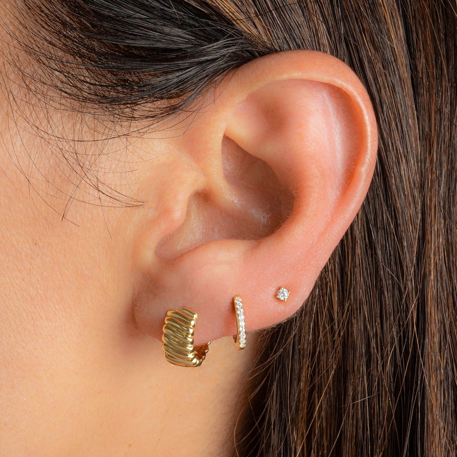 gold huggie earrings featuring a wavy pattern paired with a thin diamond huggie and a solitaire stud earrings