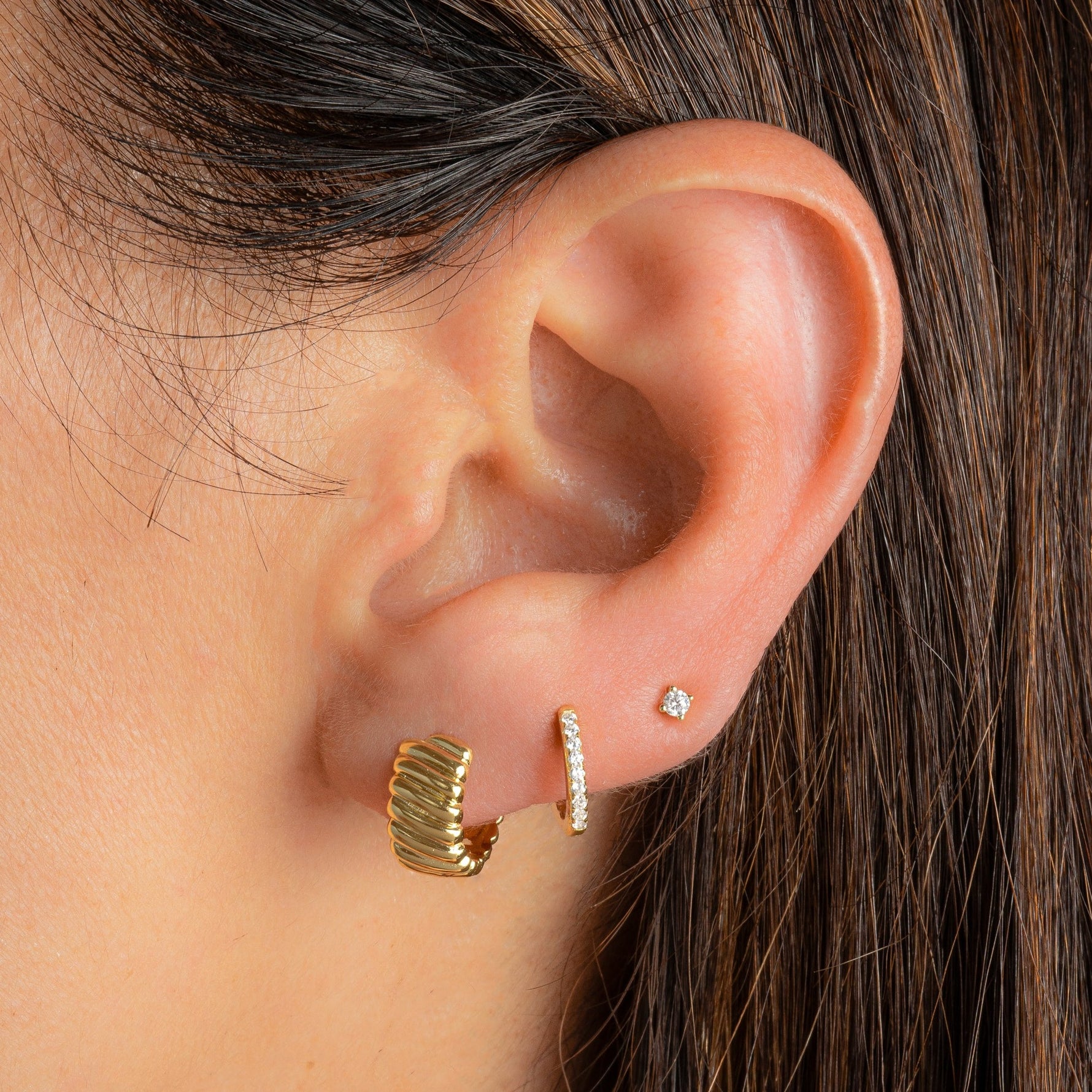 gold huggie earrings featuring a wavy pattern paired with a thin diamond huggie and a solitaire stud earrings
