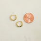 Close up flat-lay image of minimalist earrings. The gold baby huggie earrings are being compared to the size of a penny. 