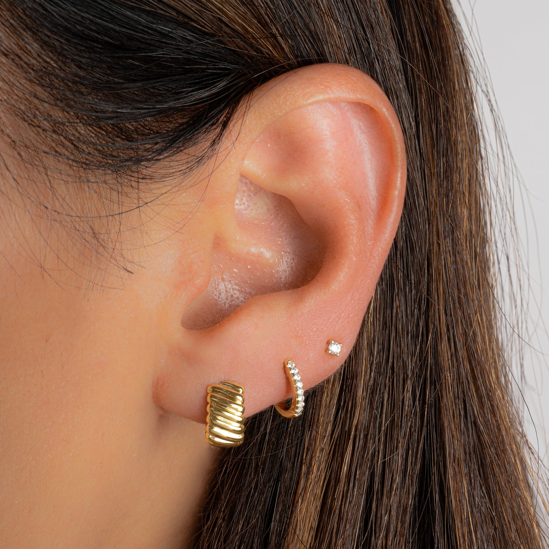 a model wearing a gold huggie hoop earring, diamond huggies and a diamond stud made with cubic zirconia