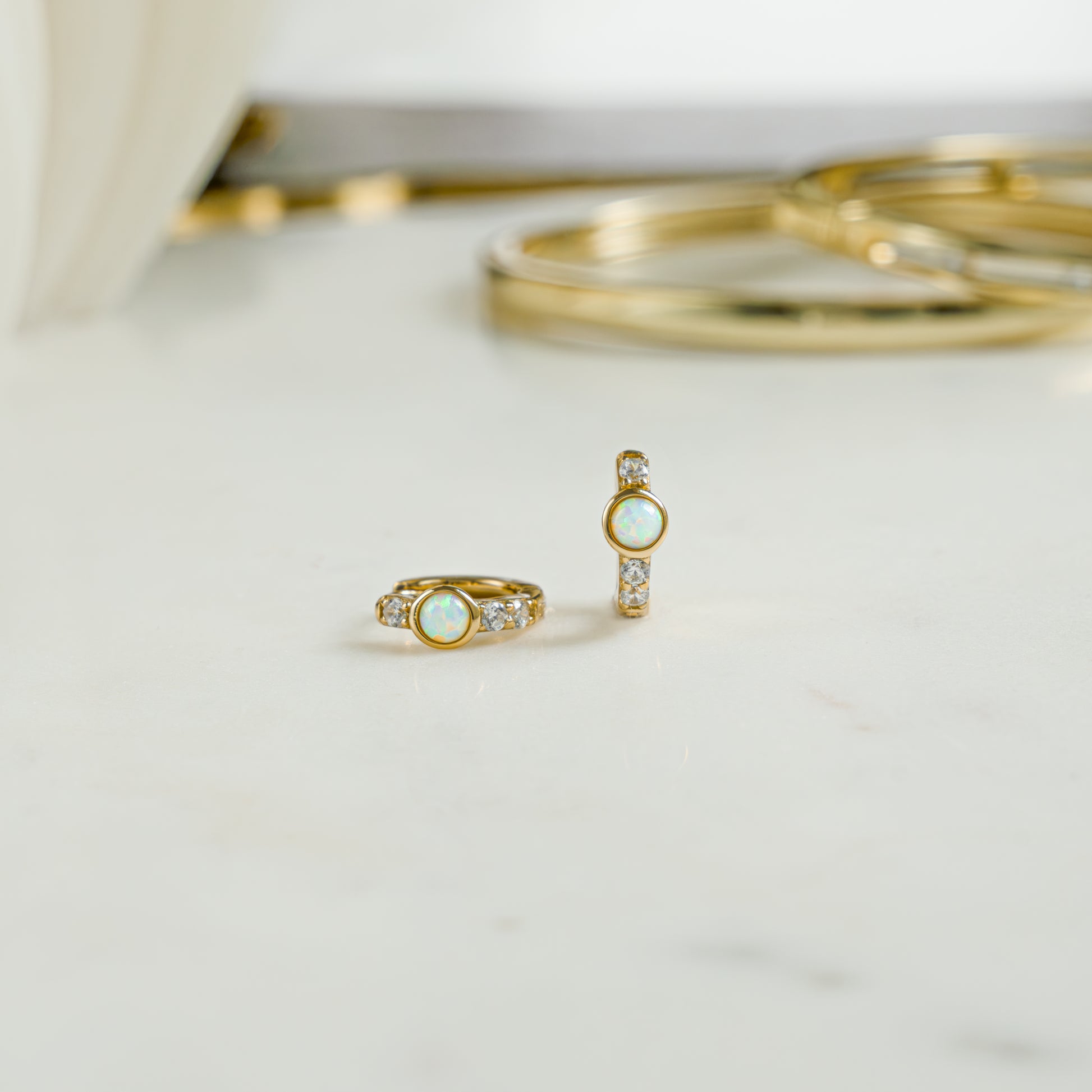 Close up image of gold studded cz opal earrings. The aesthetic earrings feature a solitaire opal stone and cz diamonds. Perfect gift for an october birthday.