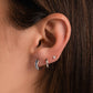 Model wearing silver aquamarine huggie earrings and matching silver plain hoops in the middle and diamond stud earrings on the third piercing. 