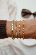 Gold solid bangle bracelet from Sami Jewels worn as part of a bracelet stack on a model's wrist.