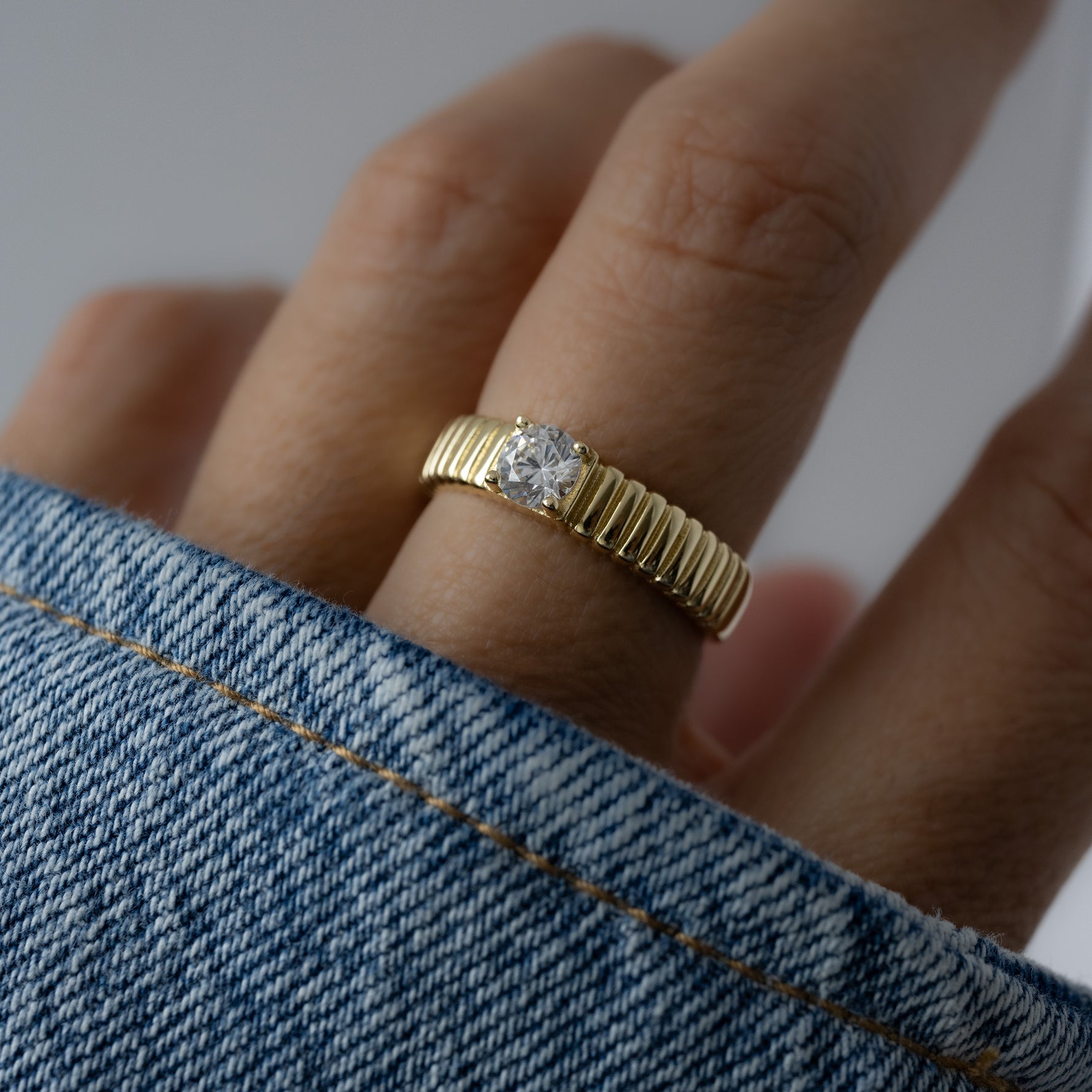 model wearing a dainty ring with a fluted gold band, adding subtle depth and dimension to the classic solitaire ring setting.