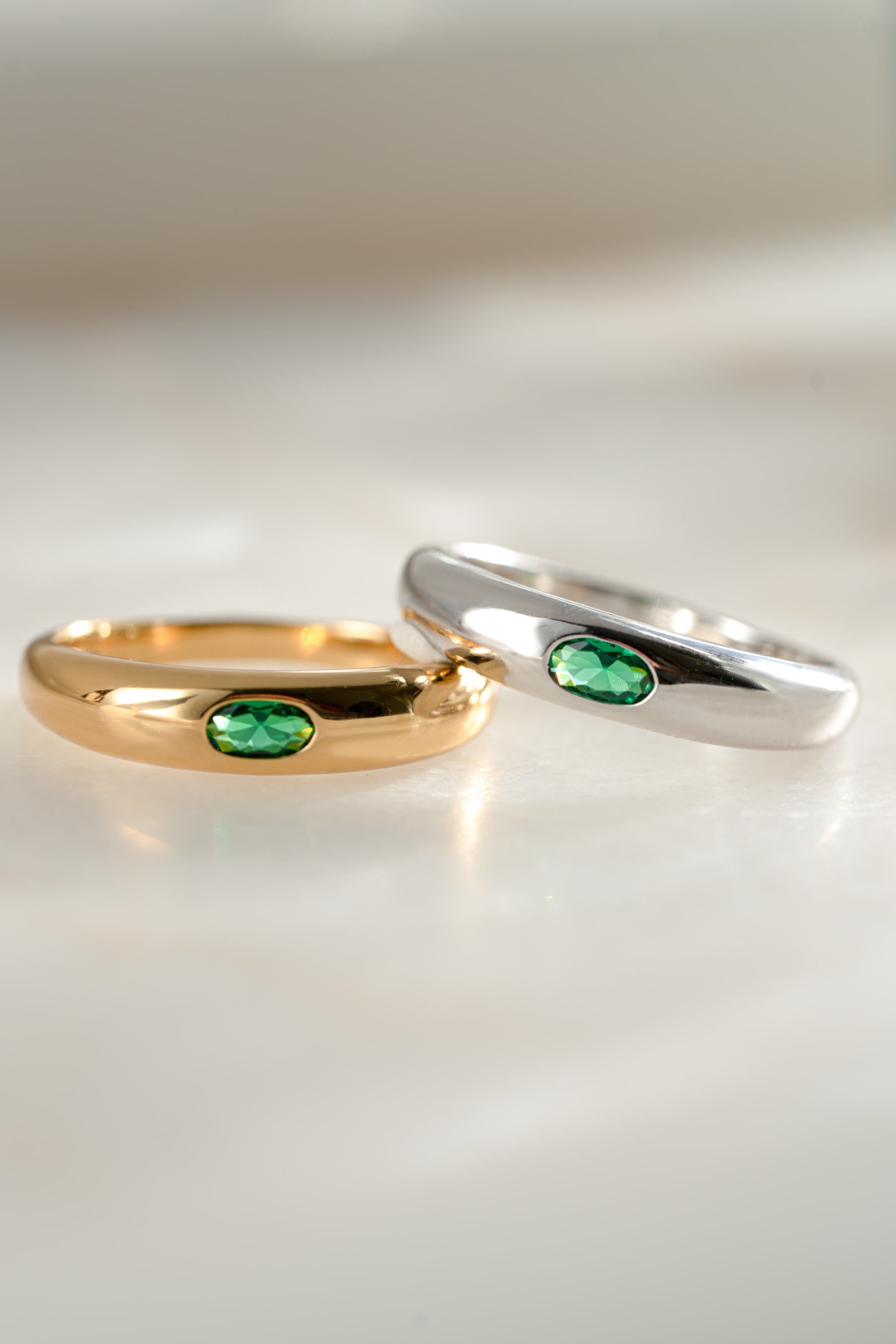 two bezeled emerald dome rings, one gold dome ring, and one sterling silver dome ring laying next to eachother
