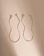 Two silver bracelets laid side by side, showing their lobster clasps, extenders and heart-shaped tags.