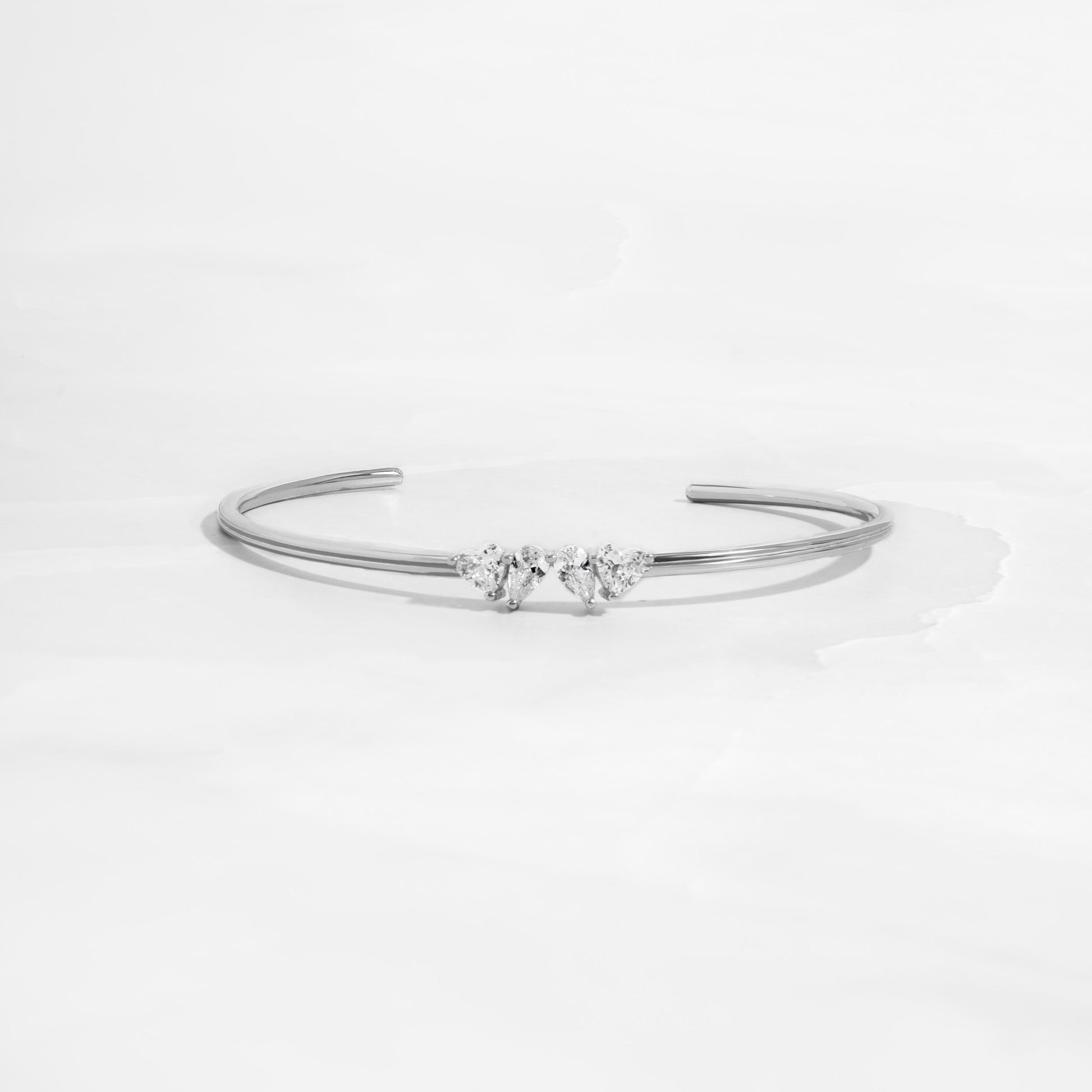 Flat lay of a silver cuff bracelet with heart and teardrop gemstones. 