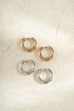 gold 10mm hoop earring and gold played hoop earring on a neutral background