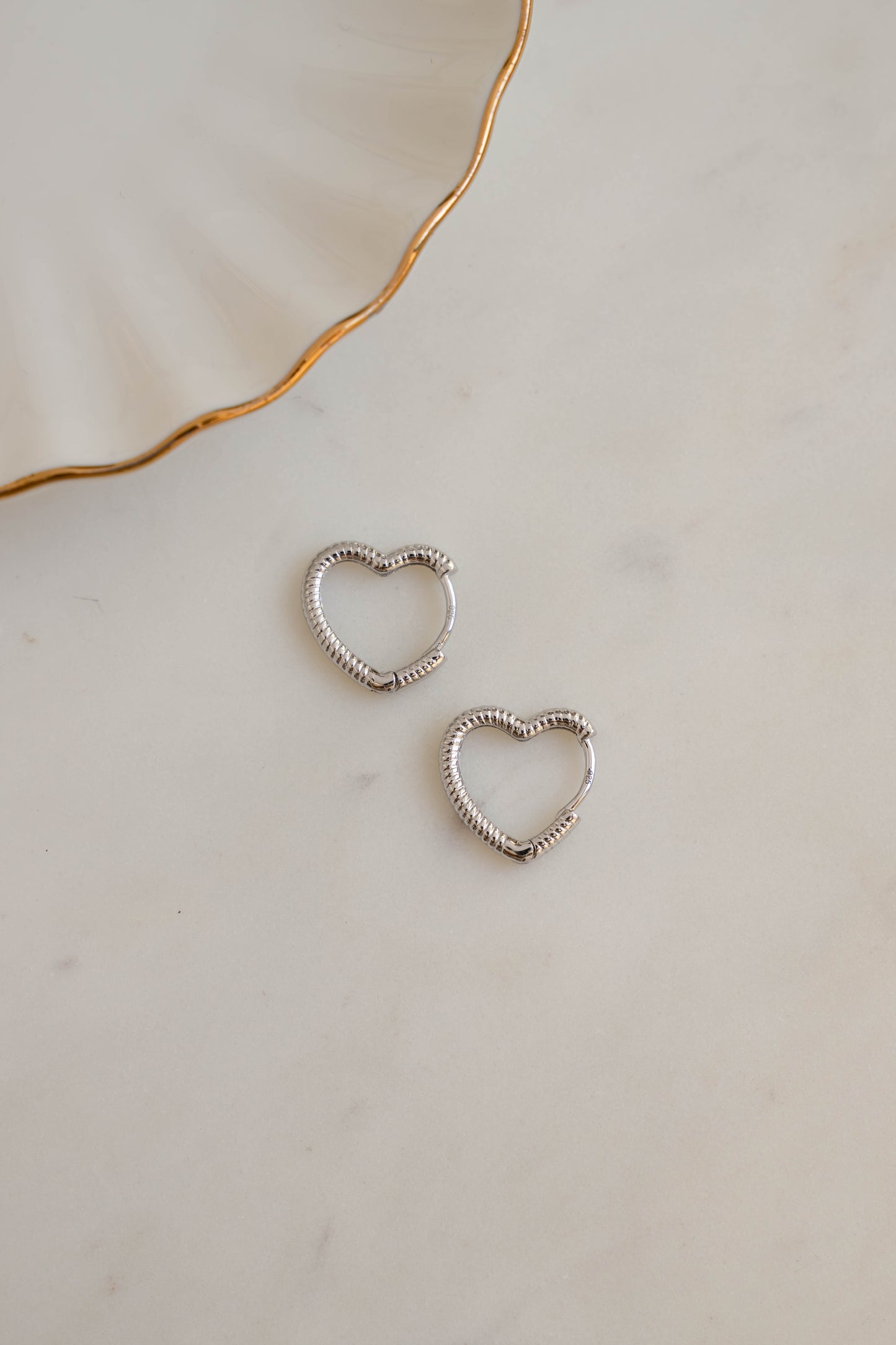 Sterling silver heart hoop earrings on white marble background