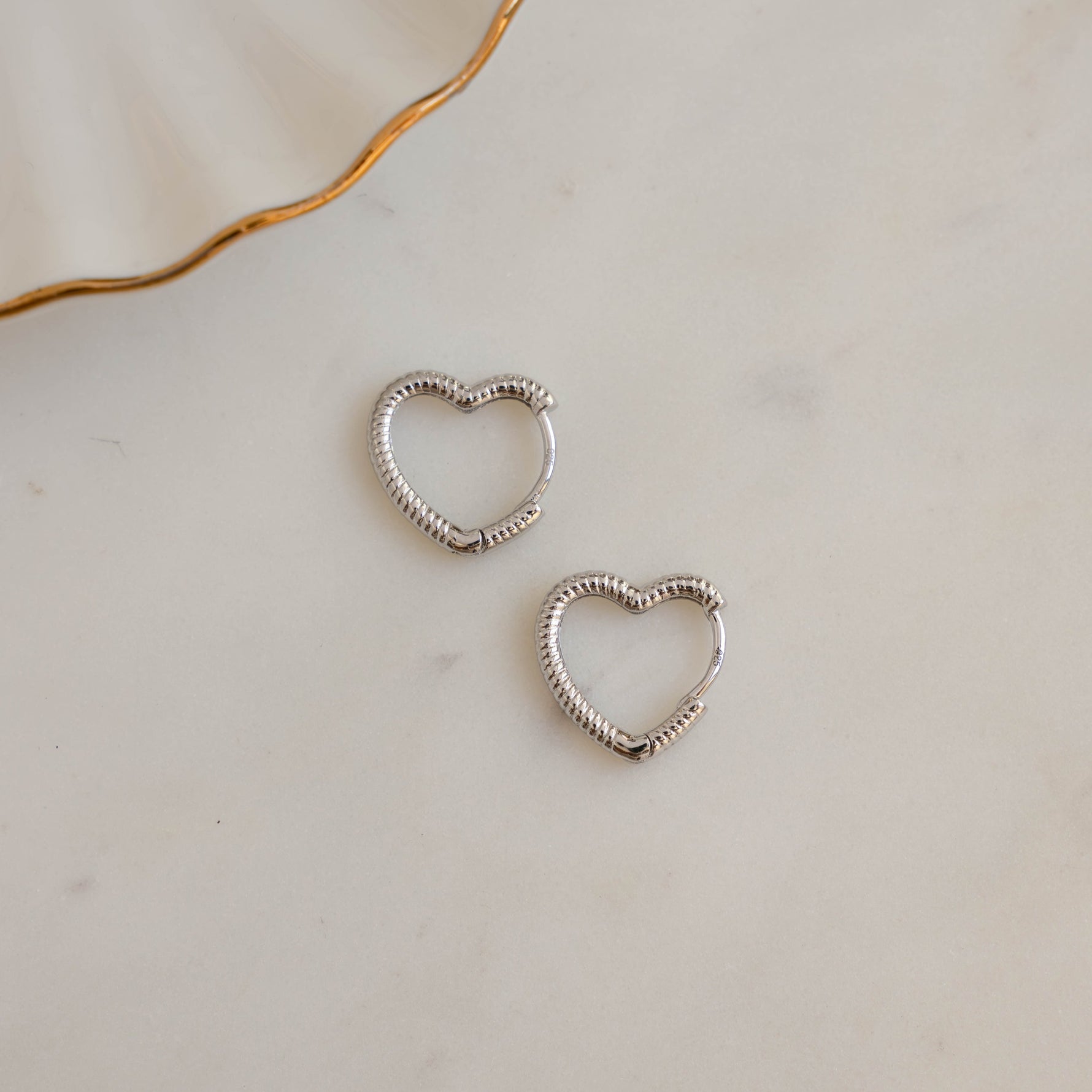 Sterling silver heart hoop earrings on white marble background