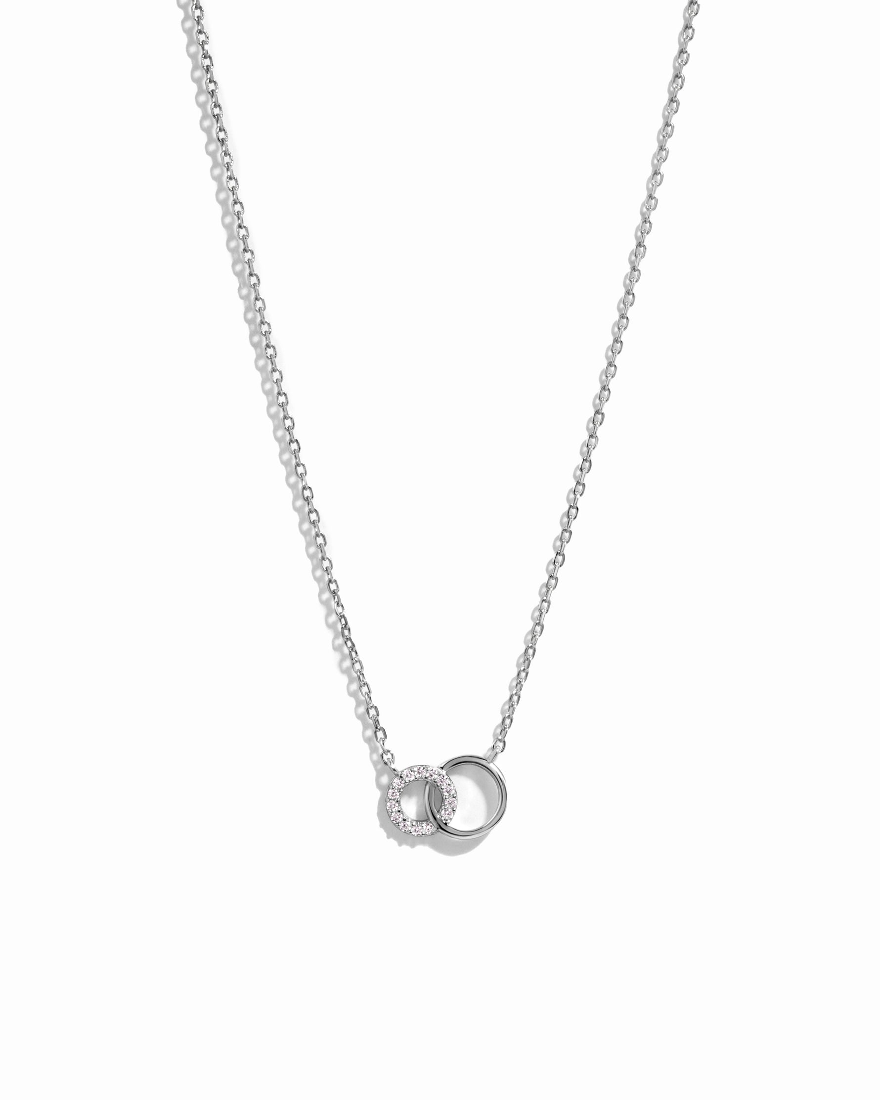 Dainty silver necklace with interlocking infinity circle pendant, with tiny diamond accents on delicate silver chain against a white background