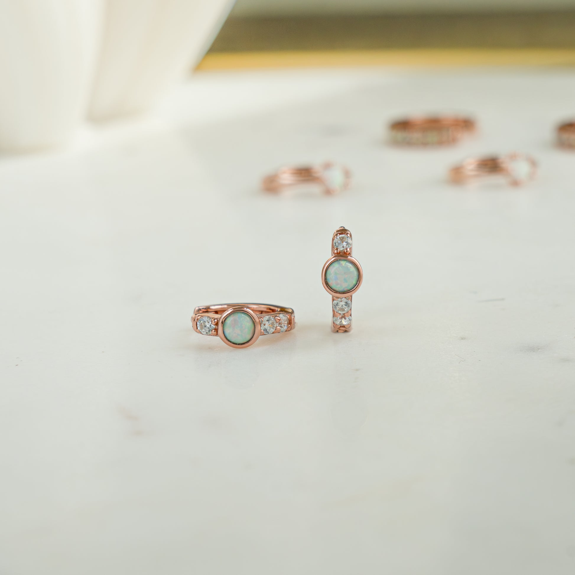 Close up image of rose gold tiny huggie earrings. The opal hoop earrings feature cz diamonds with a solitaire opal stone. 