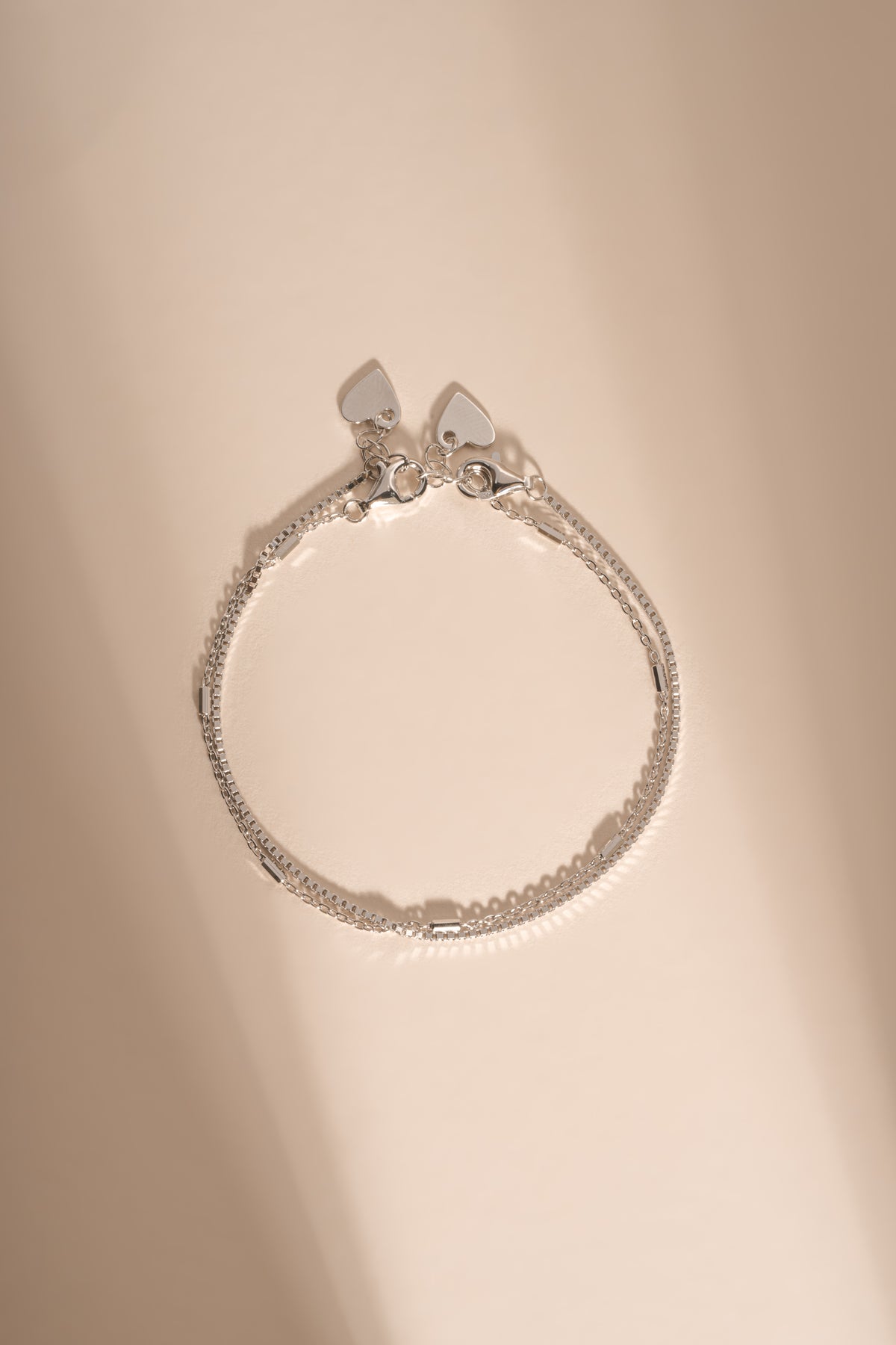 Silver box chain and satellite bracelets arranged together on a cream background.