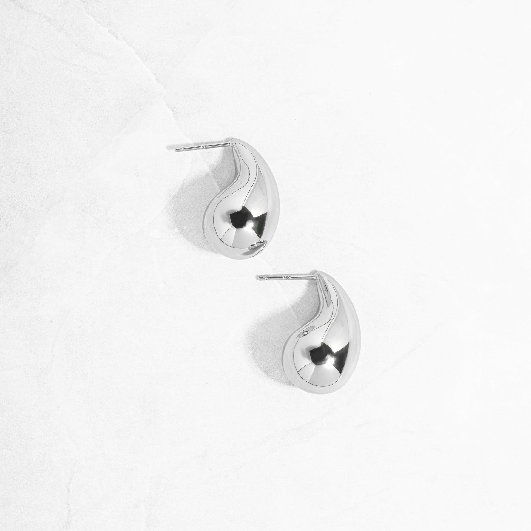 flat lay of  drop earrings, set in sterling silver, featuring a thick, rounded teardrop form, solid yet smooth. 