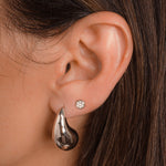 model wearing bold teardrop earrings,  set in silver, thick yet feather-light, with a sleek, high-shine finish. layered with silver stud earrings