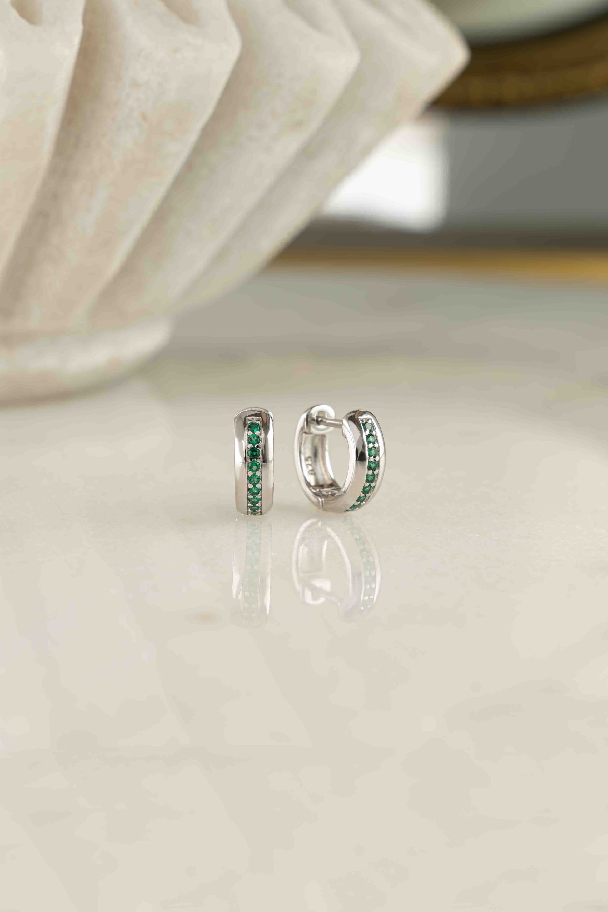 a pair of sterling silver tiny hoop earrings featuring a striped emerald band down the center