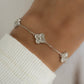 Close-up of a clover jewelry charm bracelet worn on model’s wrist.