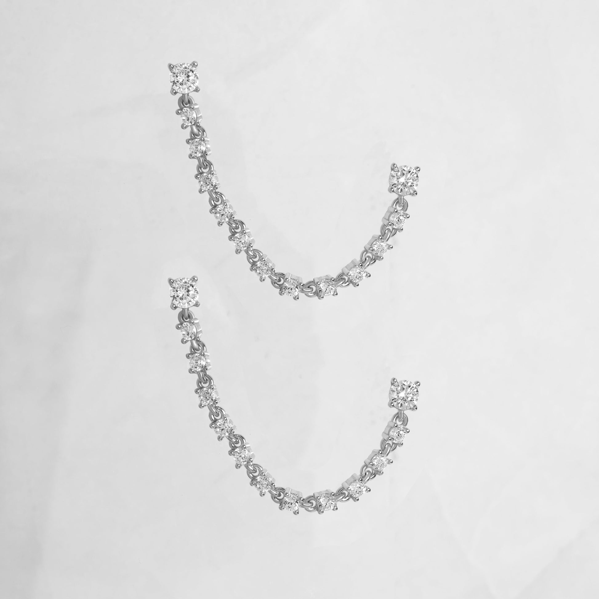 close up of silver earrings with double piercing diamond tennis chain.