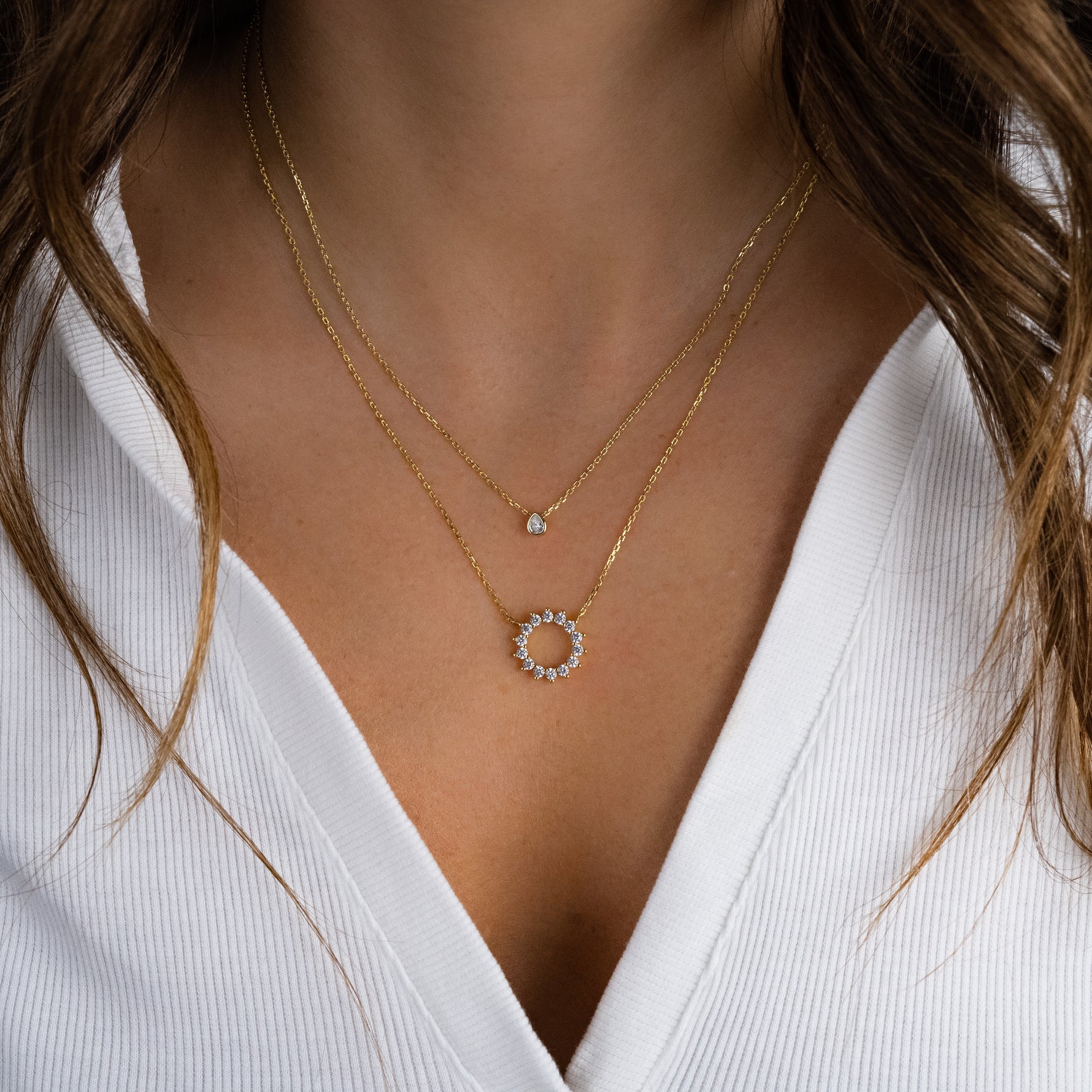 Gold sunburst necklace styled on model wearing white casual shirt, dainty and delicate necklace stack