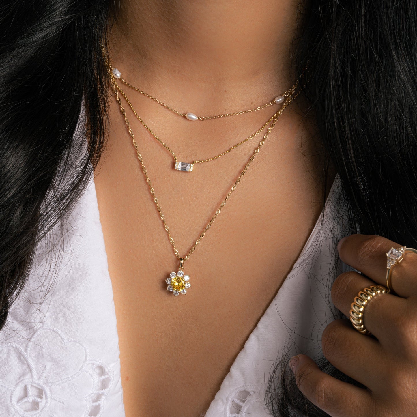 model wearing a sunflower necklace, a baguette necklace and a beaded pearl necklace stacked together