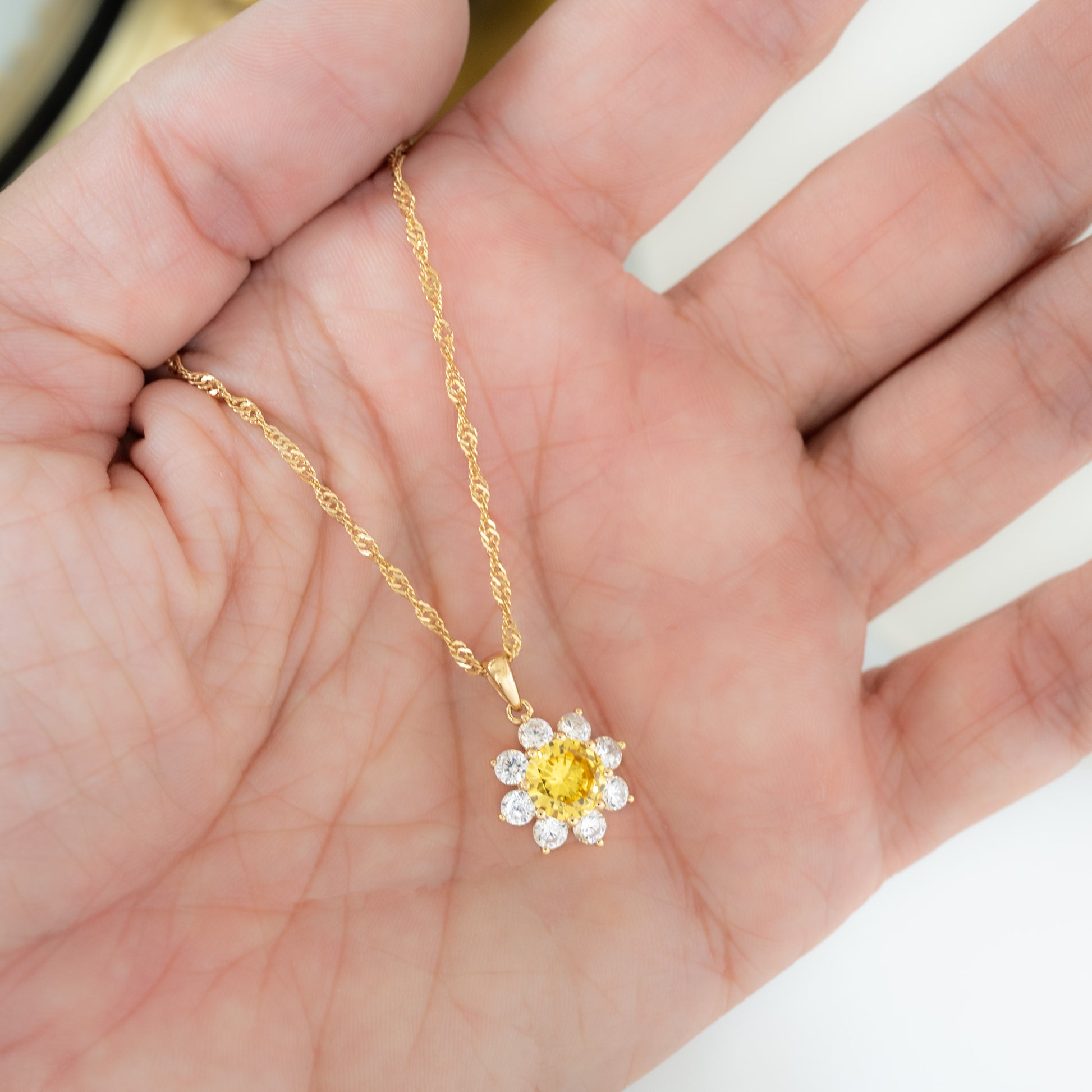 a model's hand holding a sunflower necklace 