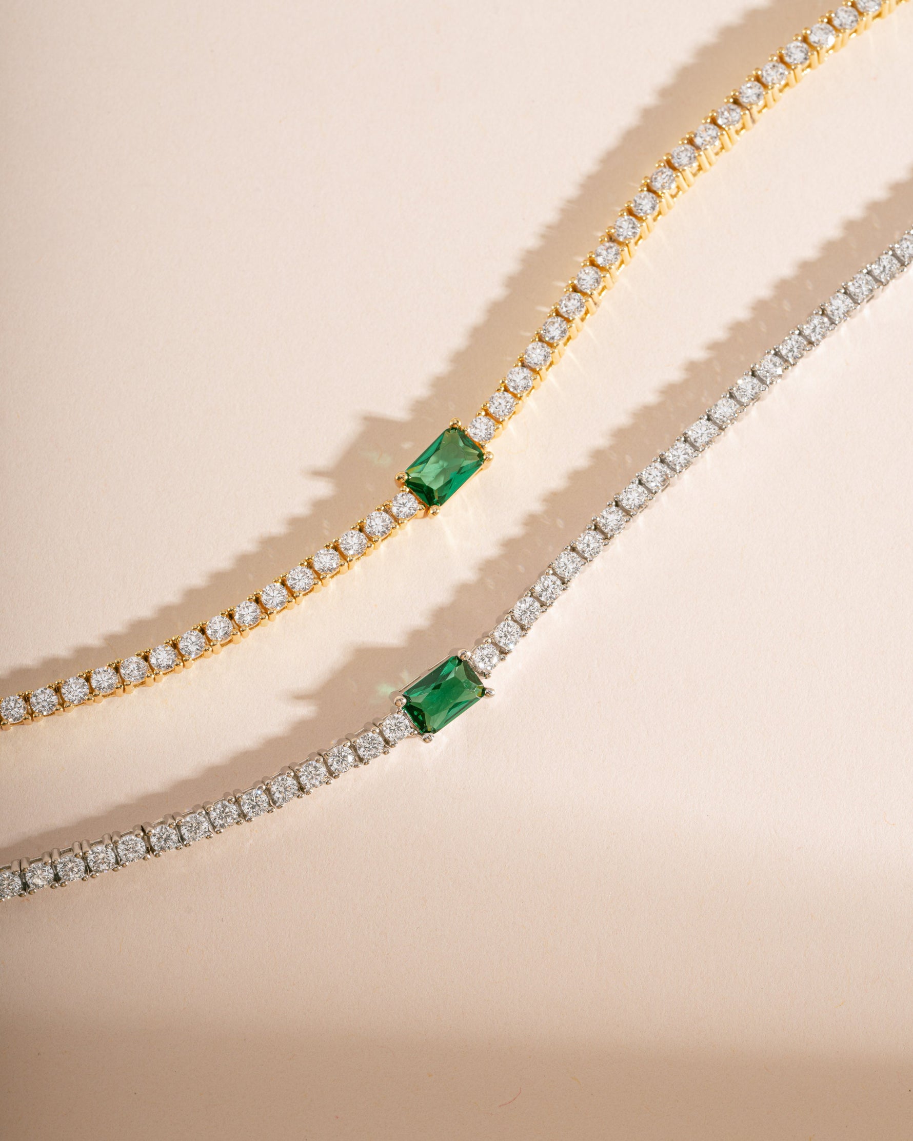 Gold and silver tennis bracelet with emerald baguette charm by Sami Jewels, featuring sparkling gemstones and elegant design.