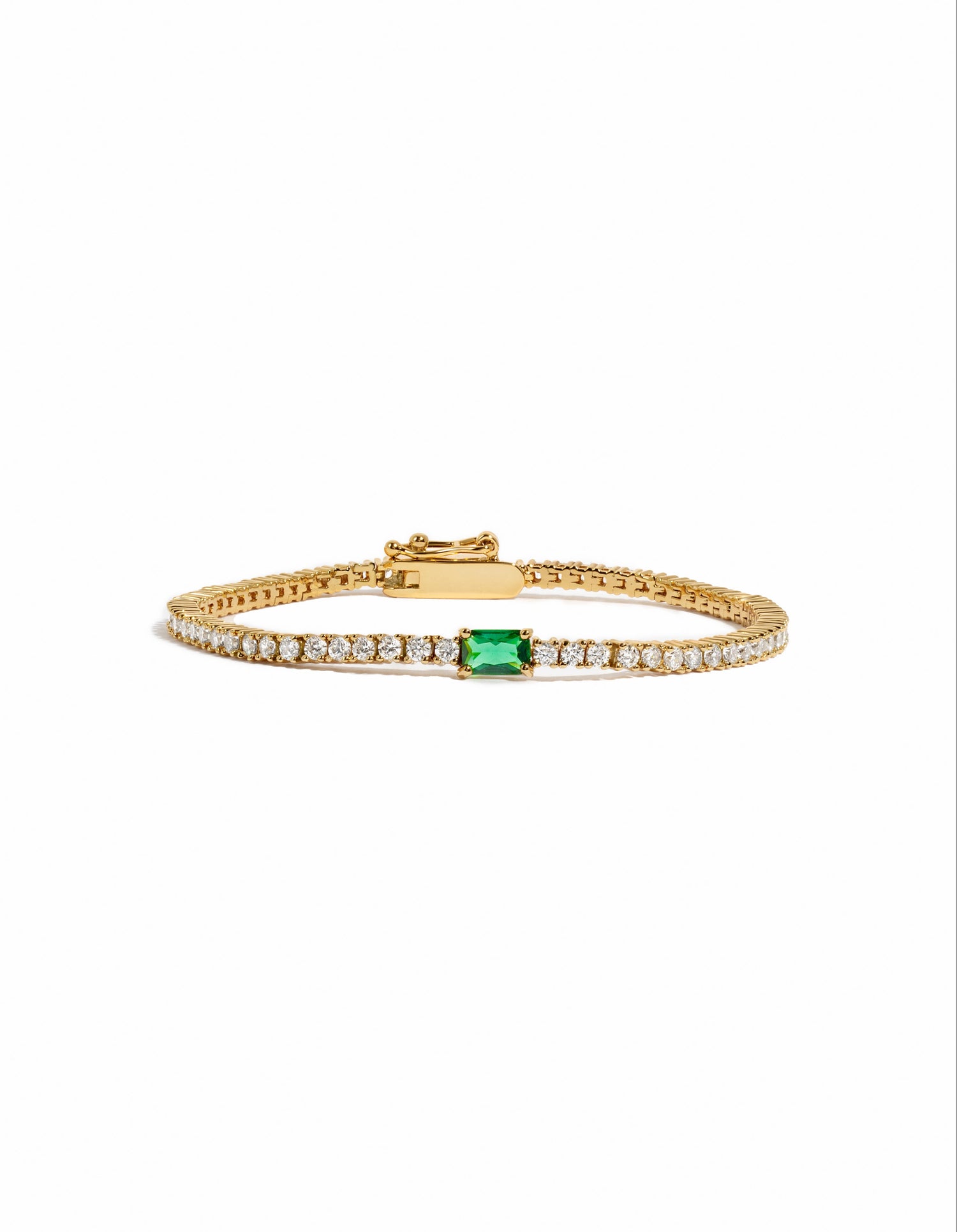 Gold tennis bracelet with emerald baguette charm from Sami Jewels, featuring sparkling stones on a clean white background.