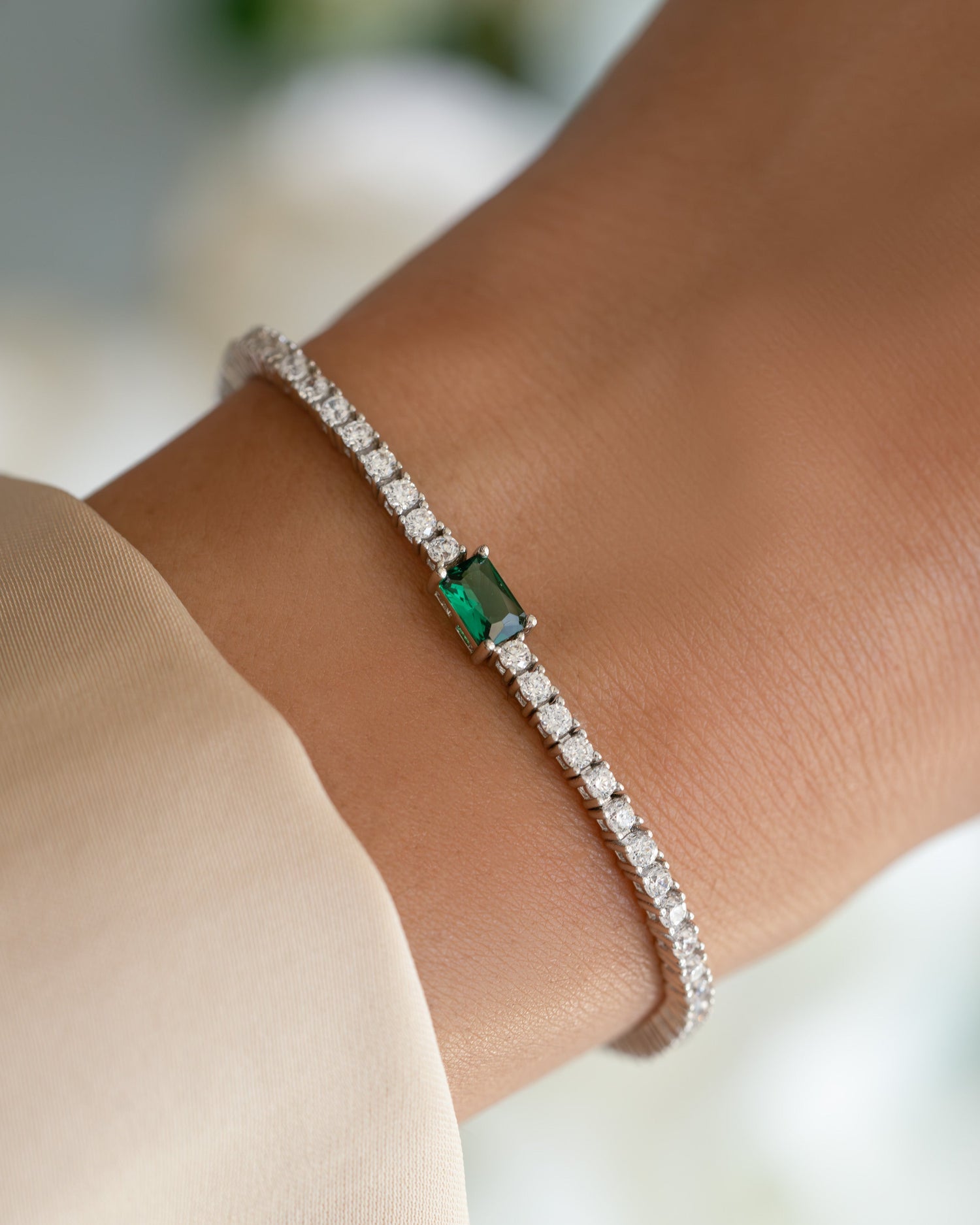 Silver tennis bracelet featuring an emerald baguette charm, showcasing elegant jewelry design by SJ Faire.