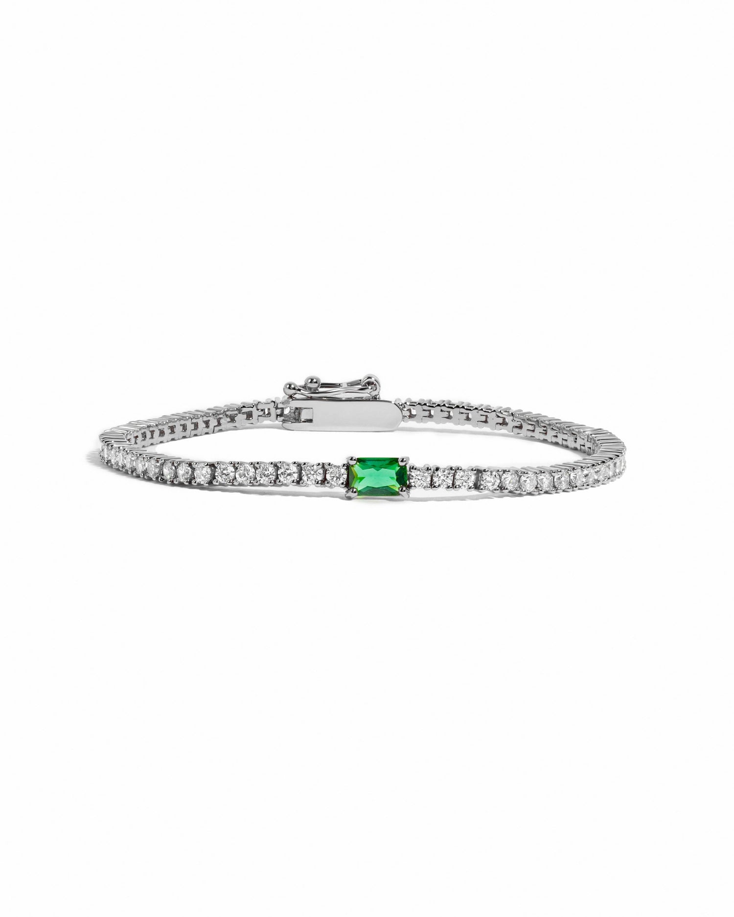 Silver tennis bracelet with emerald baguette charm, featuring a sleek design and sparkling stones, on a white background.