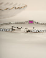 Silver tennis bracelet by Sami Jewels featuring a ruby baguette charm and box clasp closure.