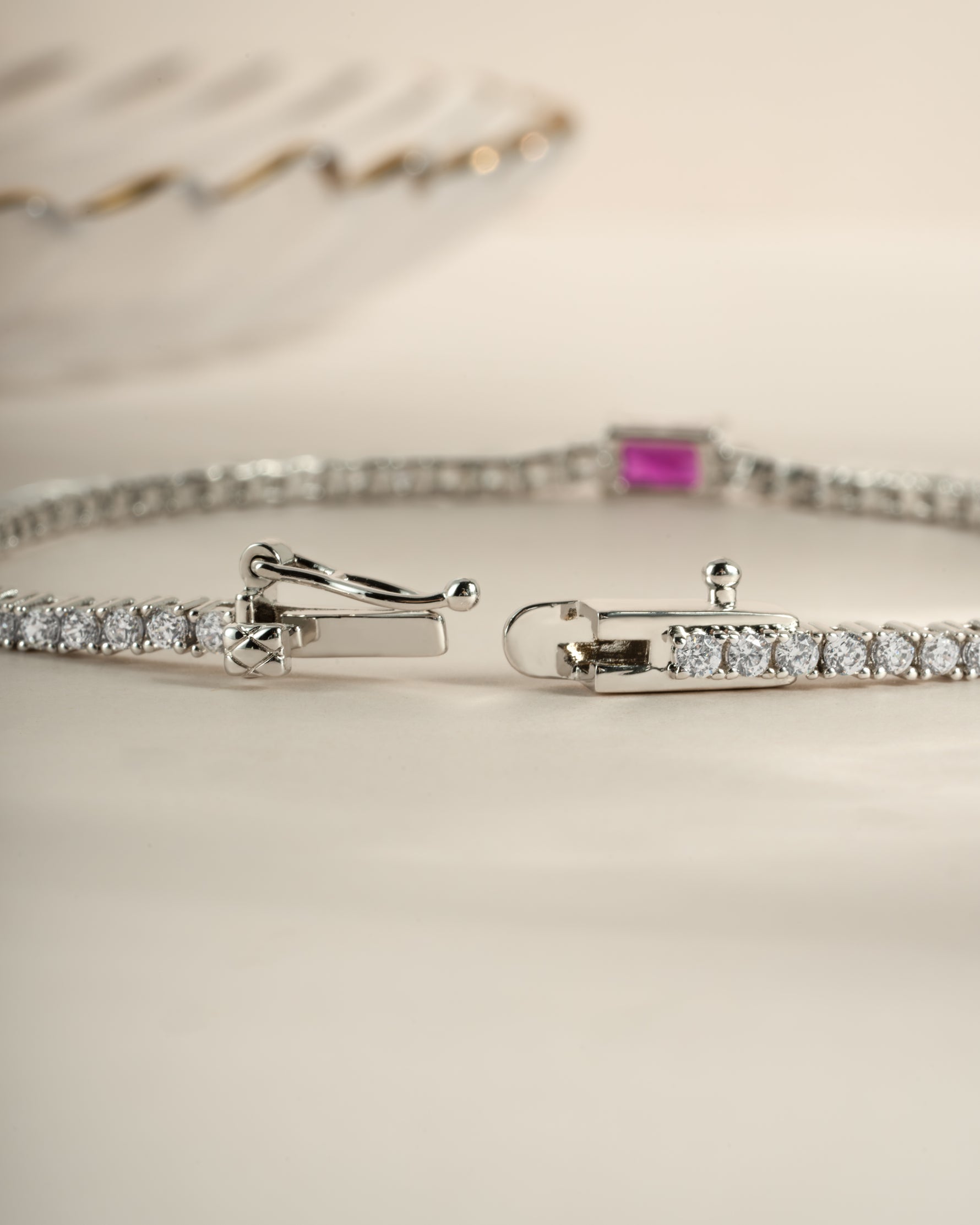 Silver tennis bracelet by Sami Jewels featuring a ruby baguette charm and box clasp closure.