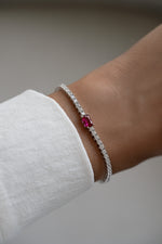 Silver tennis bracelet with ruby baguette charm from Sami Jewels showcasing elegant jewelry design.
