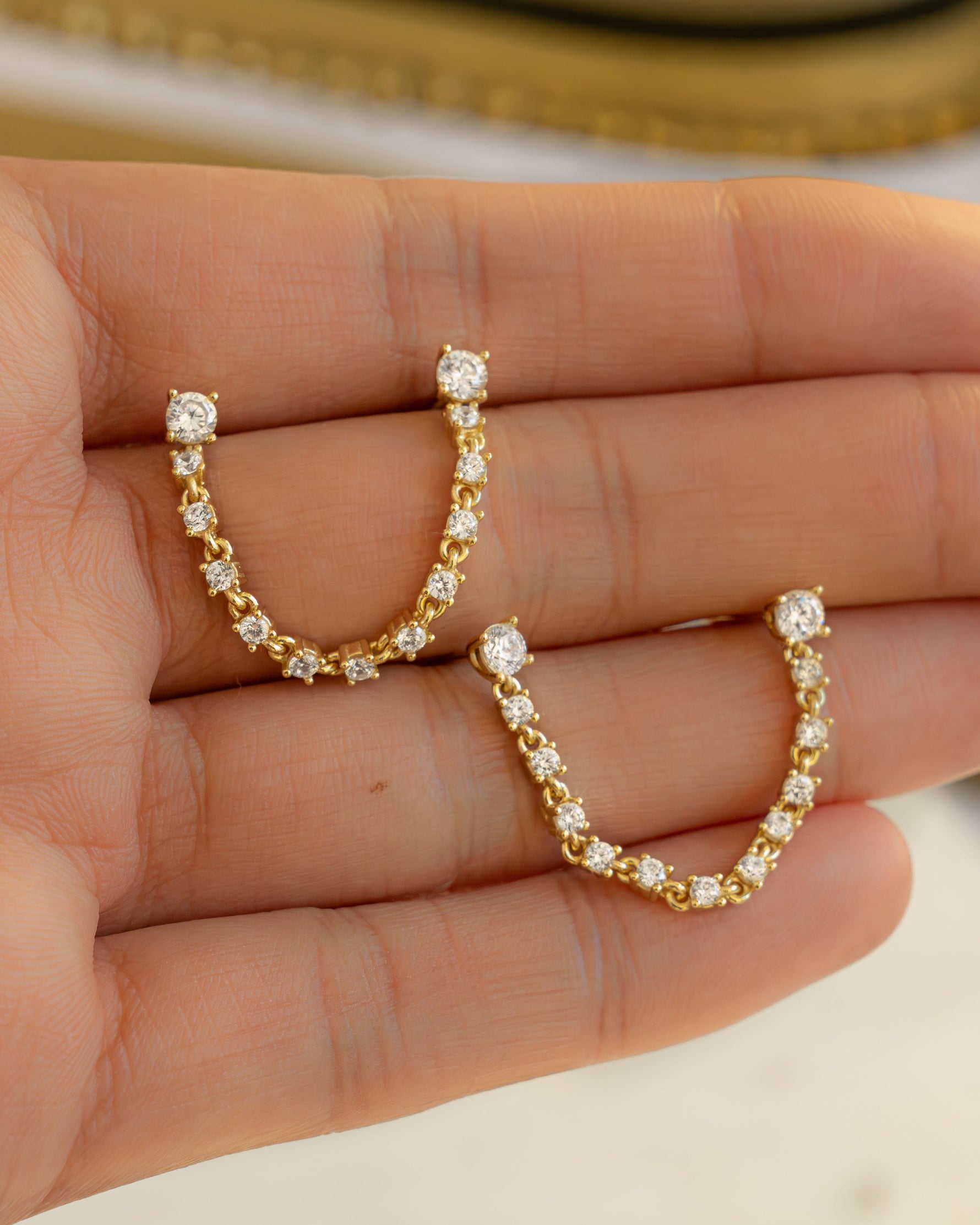 held on hand, a close up of a  pair of diamond-studded gold earrings for Double piercing