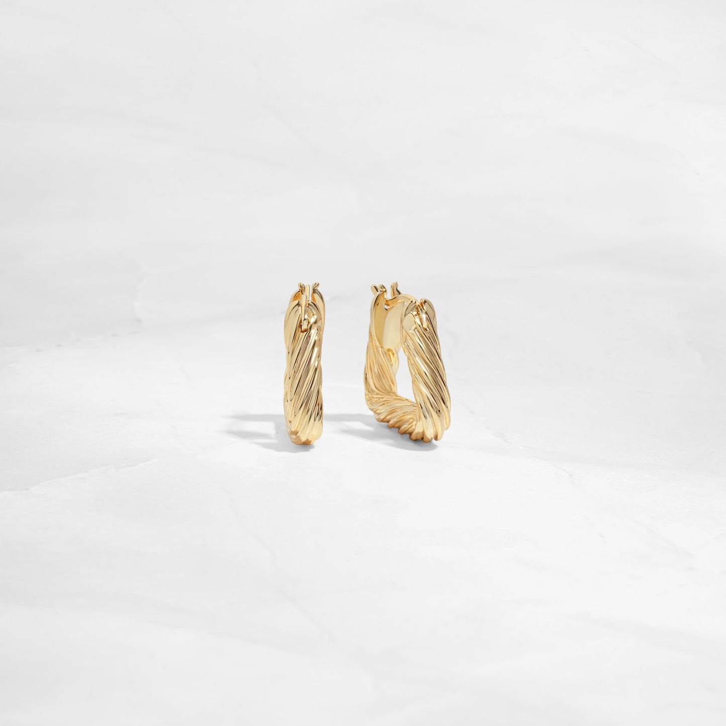 Side and front profile of chunky gold hoop earrings with a geometric design.